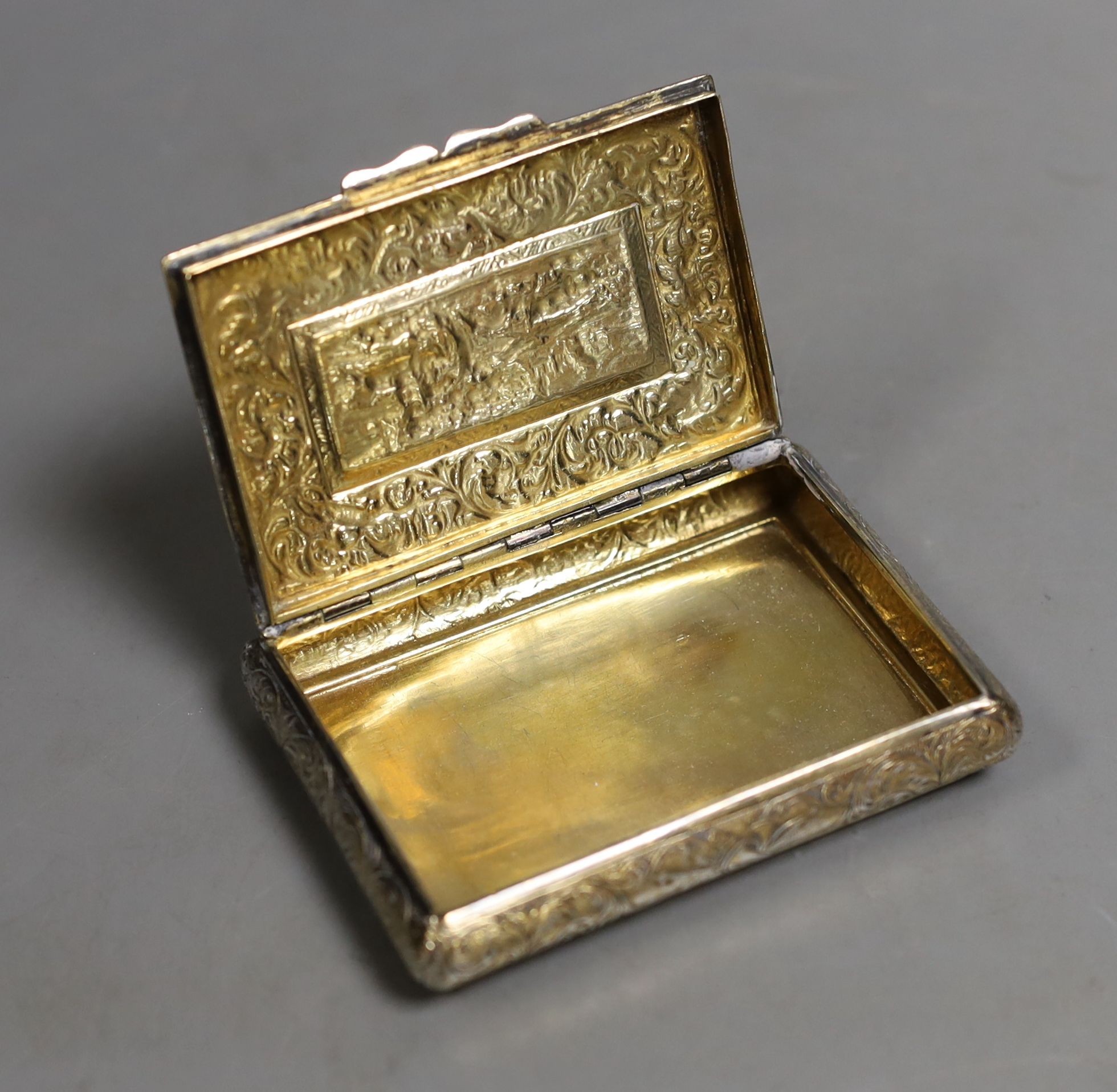 A 19th century continental gilt white metal rectangular bombe shaped snuff box, embossed with foliate scrolls and central stag hunting scene, unmarked, 81mm.